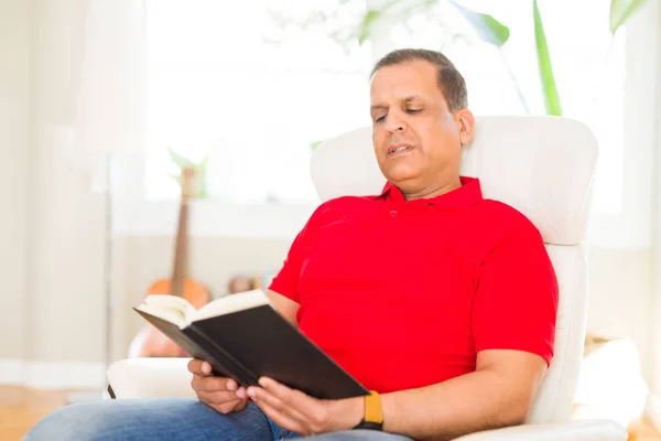 Orta yaş erkek evde kanepede oturan bir kitap okuma — Stok fotoğraf