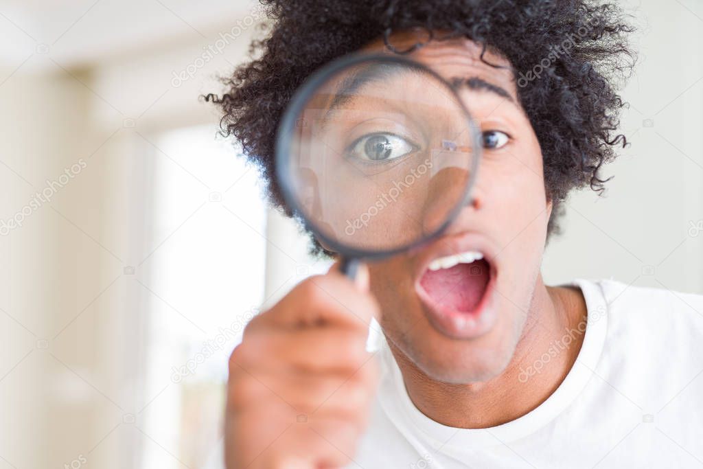 African American man looking through magnifying glass scared in shock with a surprise face, afraid and excited with fear expression