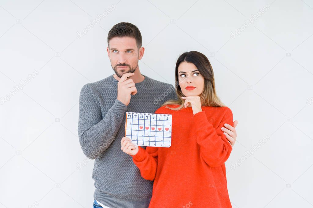 Young couple holding ovulation calendar over isolated background serious face thinking about question, very confused idea