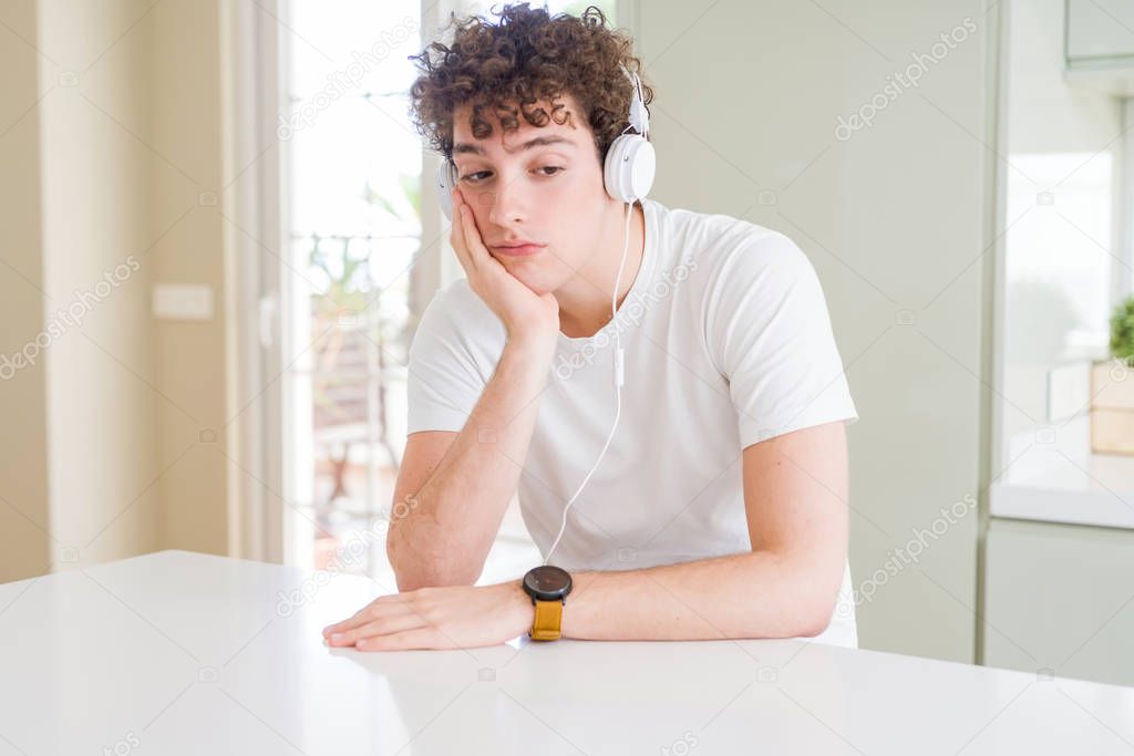 Young man listening to music wearing headphones at homes thinking looking tired and bored with depression problems with crossed arms.
