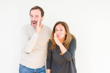 Beautiful middle age couple in love over isolated background hand on mouth telling secret rumor, whispering malicious talk conversation