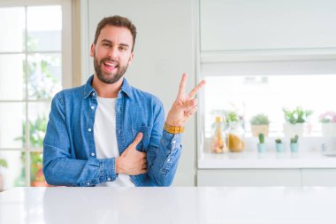 Yakışıklı adam evde mutlu yüz zafer işareti yaparken kameraya göz kırpıyor ile gülümseyen. İki numaralı.