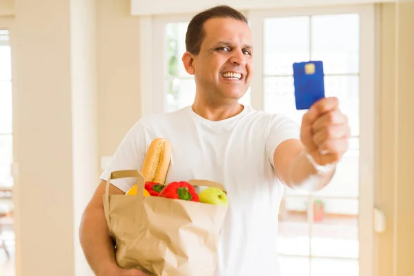 Homme d'âge moyen tenant sac d'épicerie et montrant carte de crédit — Photo