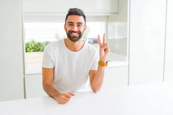 英俊的西班牙男子随意白色 T恤在家里微笑着 高兴的脸在相机眨眼做胜利的标志 — 图库照片