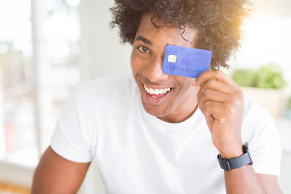 African American man holding credit card with a happy face standing and smiling with a confident smile showing teeth