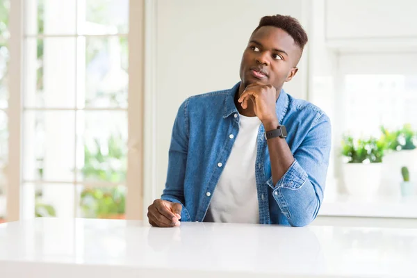 Handsome african american man at home with hand on chin thinking about question, pensive expression. Smiling with thoughtful face. Doubt concept.