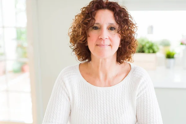 Beautiful senior woman wearing white sweater at home Relaxed with serious expression on face. Simple and natural with crossed arms