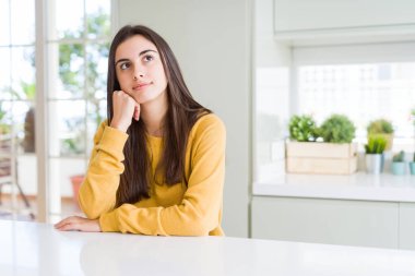 Çene düşünme hakkında soru, dalgın ifade üzerine el ile sarı kazak giyen güzel genç kadın. Düşünceli yüzüyle gülümsüyor. Şüphe kavramı.