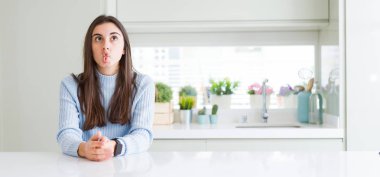 Beyaz ev yapma balık yüz dudaklı, çılgın ve komik bir jest masada oturan güzel genç kadın geniş açı resim. Komik ifade.