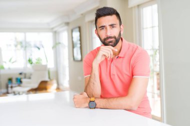 Çene düşünme hakkında soru, dalgın ifade üzerine el ile evde rahat t-shirt giyen İspanyol yakışıklı. Düşünceli yüzüyle gülümsüyor. Şüphe kavramı.