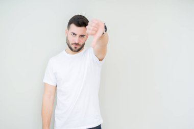 Mutsuz ve kızgın ret gösterilen ve başparmak aşağı hareketi ile negatif seyir izole arka plan üzerinde rahat beyaz t-shirt giyen genç yakışıklı adam. Kötü ifade.