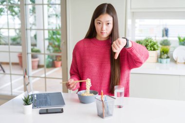 Güzel Asyalı kadın çalışma kullanma laptop ve kızgın yüzü ile Asya .erişte yiyorlar, eksi işareti gösterilen sevmemek başparmak aşağı, ret kavramı ile