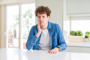 Evde rahat denim ceket giyen genç yakışıklı adam acı ifadesi ile el ile ağız diş ağrısı veya dişlerde dişlerle ilgili hastalık nedeniyle dokunmadan. Diş hekimi kavramı.