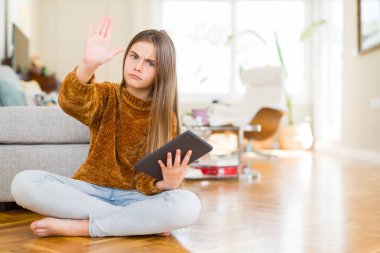 Güzel genç kız çocuk açık eliyle dur işareti ile ciddi ve kendine güvenen ifade, savunma jest yapıyor katta oturan dijital dokunmatik tablet kullanma