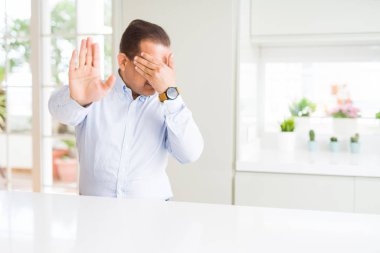 Orta yaş adam evde el kapsayan gözlerle oturan ve stop jest ile acı ve korku ifadesi. Utandım ve negatif kavramı.