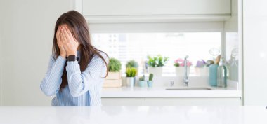 Geniş açı resim güzel genç kadın ağlayarak süre elleriyle yüzünü kapsayan üzgün ifade ile evde beyaz masaya oturuyordu. Depresyon kavramı.