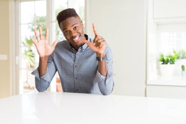 Afro-Amerikan yakışıklı gösteren ve parmakları ile işaret beyaz masada kendinden emin ve mutlu gülümseyerek süre yedi numara.