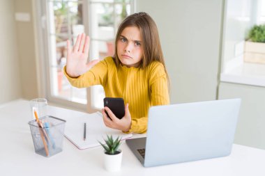 Güzel genç kız çocuk açık eliyle dur işareti ile ciddi ve kendine güvenen ifade, savunma jest yapıyor akıllı telefon ve bilgisayar dizüstü bilgisayar kullanarak