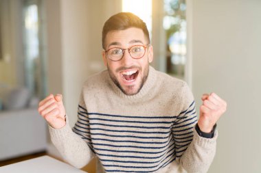 Evde gözlüklü genç yakışıklı adam şaşırmış ve başarı için hayran kaldırdı kollarını açarak kutluyor ve gözleri açık. Kazanan kavramı.
