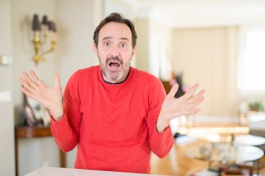 Yakışıklı orta yaş adam ev clueless ve şaşkın bir ifadeyle kollar ve eller kaldırdı. Şüphe kavramı.