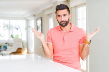 Yakışıklı İspanyol giyiyor rahat t-shirt ev clueless ve şaşkın bir ifadeyle kollar ve eller kaldırdı, dostum. Şüphe kavramı.