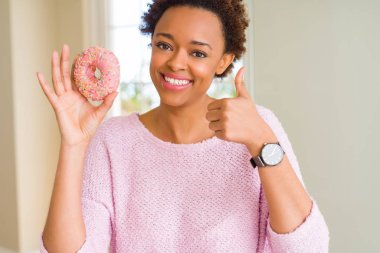 Pembe şeker çörek mutlu yeme ok işareti, başparmak ile parmak, mükemmel işareti yapıyor kocaman bir gülümseme ile genç Afro-Amerikan kadın