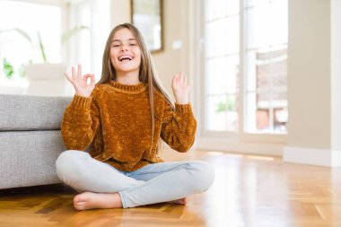 Güzel genç kız çocuk evde katta oturan rahatla ve gülümseyen gözlerle parmak ile meditasyon jest yapıyor kapalı. Yoga kavramı.