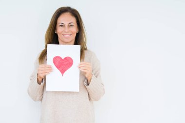 Kırmızı kalp ile kart hediye izole arka plan üzerinde duran ve diş gösterilen kendine güvenen bir gülümsemeyle gülümseyerek mutlu bir yüz ile tutan orta yaş kadın