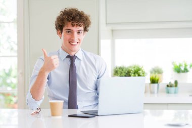 Genç iş adamı ok işareti, başparmak ile parmak, mükemmel işareti yapıyor kocaman bir gülümseme ile mutlu ofiste bilgisayar laptop ile çalışma