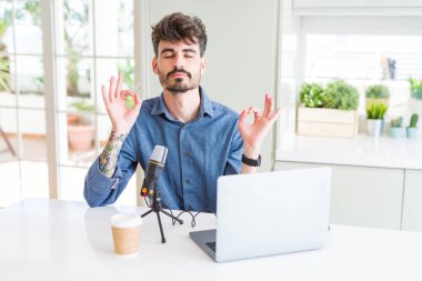 Genç adam kayıt podcast mikrofon ve bir dizüstü bilgisayar kullanarak rahatla ve gülümseyen gözlerle kapalı parmak jestle meditasyon yapıyor. Yoga kavramı.