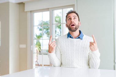 Yakışıklı adam rahat kazak giyen hayrete ve yukarıya bakıyor ve parmakları ile işaret ve silah kaldırdı şaşırttı.