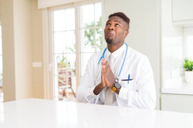 Afrikalı-Amerikalı doktor adama yalvarıyor ve umut ifade yüzünde çok duygusal ve endişe ile birlikte elleriyle dua Kliniği. Bağışlanmak. Din kavramı.