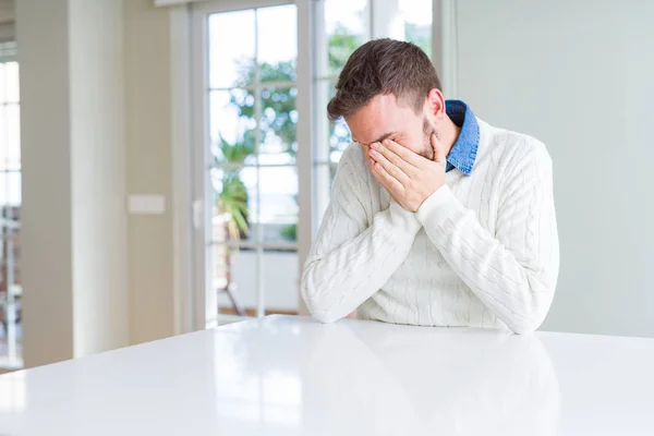 Handsome man wearing casual sweater with sad expression covering face with hands while crying. Depression concept.