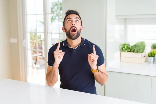 Bonito Homem Hispânico Casa Espantado Surpreso Olhando Para Cima Apontando — Fotografia de Stock