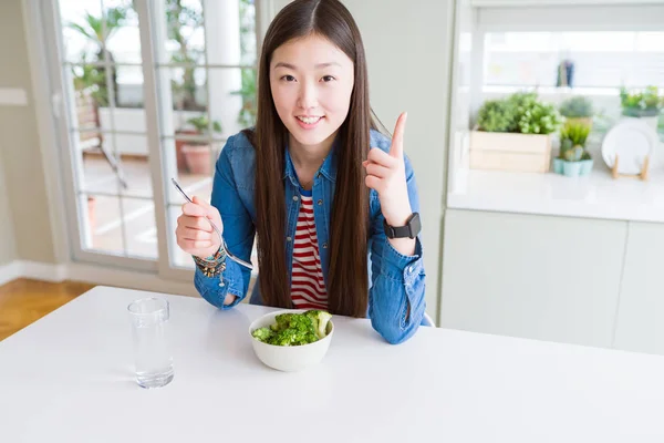 美丽的亚洲女人吃绿色新鲜花椰菜惊讶的想法或问题用快乐的脸指指点点 — 图库照片