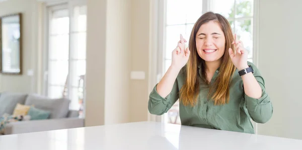 Mulher Bonita Casa Sorrindo Cruzando Dedos Com Esperança Olhos Fechados — Fotografia de Stock