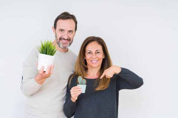 Пара средних лет держит растения на изолированном фоне с неожиданным лицом, указывающим пальцем на себя
