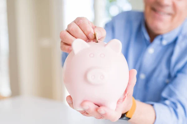 Man putting a coin inside piggy bank as savings smiling confident