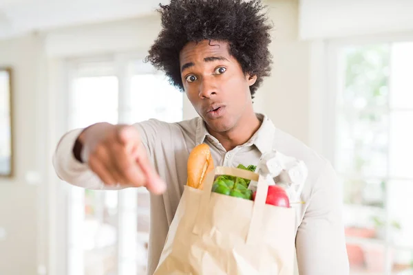 アフリカ系アメリカ人の家で新鮮な野菜の食料品袋を抱えては カメラと 正面からポジティブで自信のジェスチャーと指差し呼称 — ストック写真