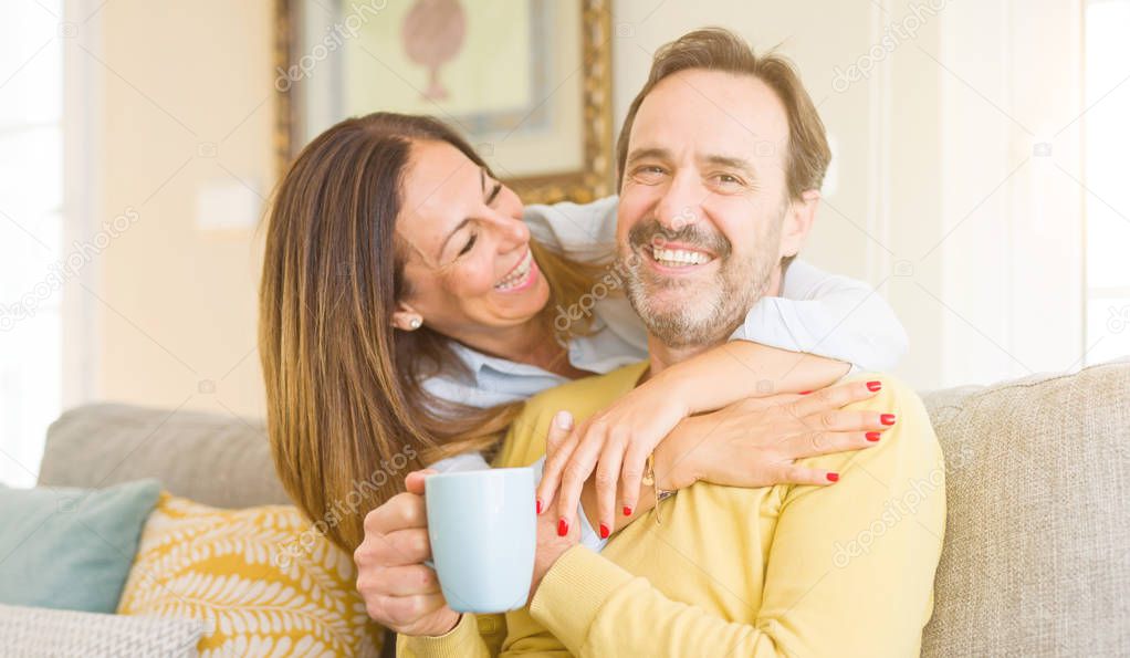 Middle age romantic couple sitting on the sofa at home drinking a cup of coffee