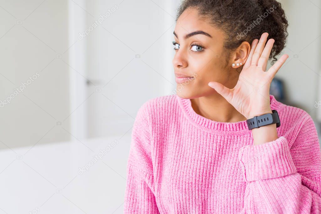 Beautiful young african american woman with afro hair smiling with hand over ear listening an hearing to rumor or gossip. Deafness concept.