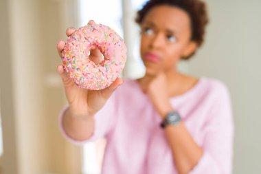 Pembe şeker çörek ciddi bir yüz düşünme hakkında soru, çok karışık fikir yeme genç Afro-Amerikan kadın