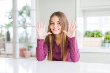 Beautiful young girl kid on white table showing and pointing up with fingers number ten while smiling confident and happy. clipart