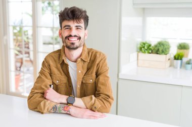 Beyaz masa mutlu yüz çapraz silah kameraya bakarak ile gülümseyerek oturan rahat ceket genç adam. Olumlu bir kişi.