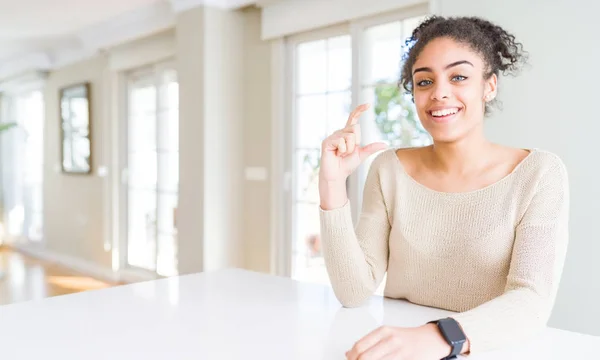 アフロ髪家で笑顔と自信を持ってテーブルの上に座って美しい若いアフリカ系アメリカ人女性は サイズ記号を見ながら指とカメラをやって手でジェスチャー 測定概念 — ストック写真