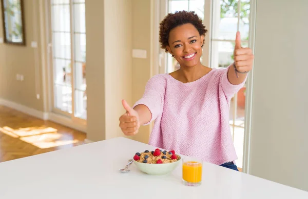 年轻的非洲裔美国妇女在早上在家里吃健康的早餐 批准用手做积极的手势 竖起大拇指微笑 为成功而高兴 看着镜头 赢家的手势 — 图库照片