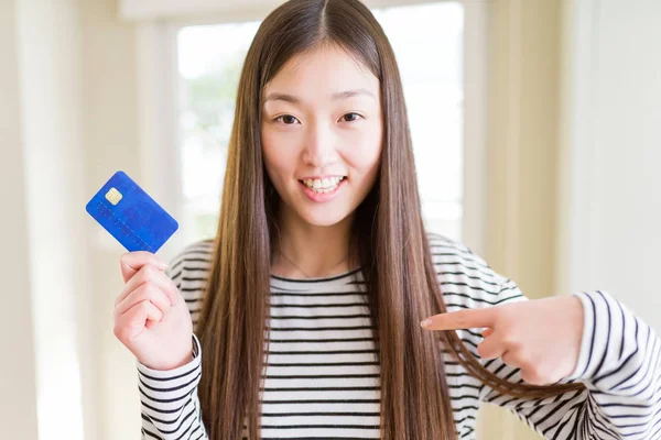 Beautiful Asian woman holding credit card with surprise face pointing finger to himself