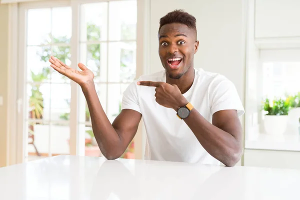 手を差し出しながら指で指して白のハンサムなアフリカ系アメリカ人表自宅驚かれるとカメラに笑顔 — ストック写真