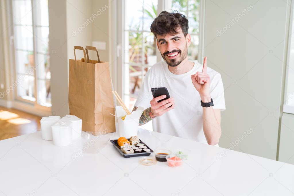 Young man eating asian sushi from home delivery and ordering food using smartphone app surprised with an idea or question pointing finger with happy face, number one