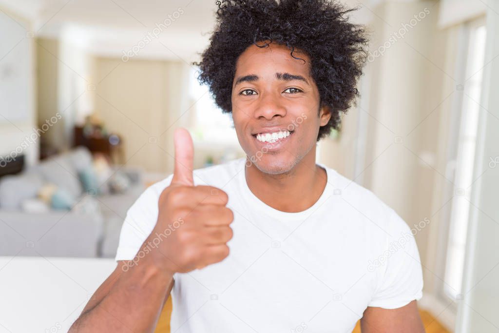 African American man at home doing happy thumbs up gesture with hand. Approving expression looking at the camera showing success.